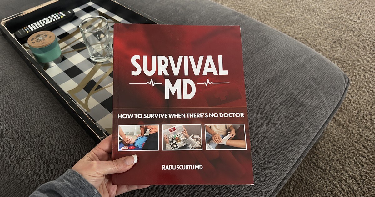 A hand holding the printed Survival MD book by Dr. Radu Scurtu over a living-room sofa