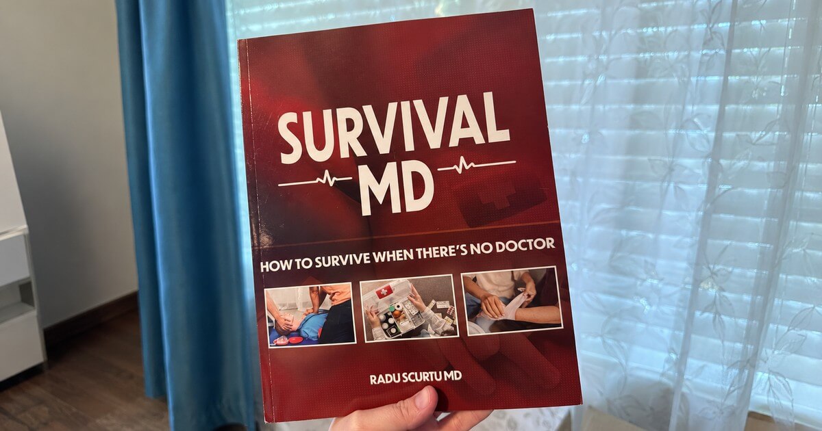 A hand holding the printed Survival MD book by Dr. Radu Scurtu in front of a window with blue curtains